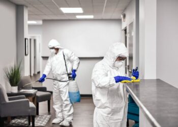 Two people in protective workwear cleaning and disinfecting offices.